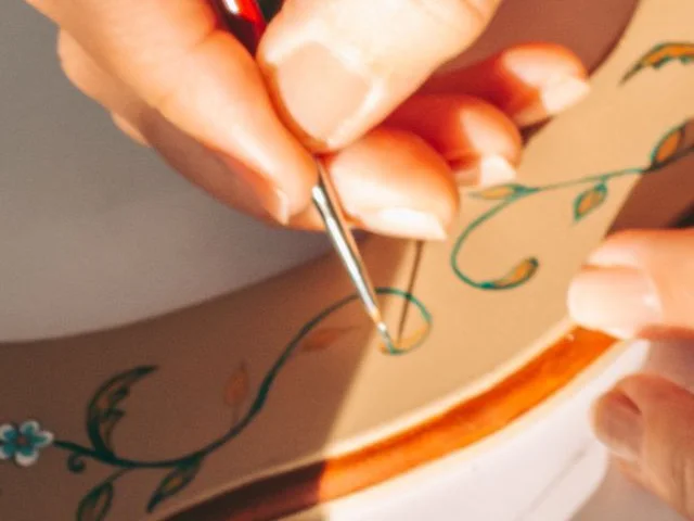 Szakember ecsettel virágos ornamentikát fest egy díszített keretre